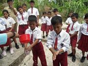 Teachers pouring water over their students' hands using dipper due to inadequate facilities for water distribution